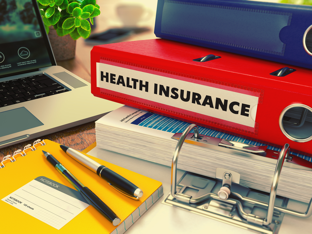 Red Office Folder with Inscription Health Insurance on Office Desktop with Office Supplies and Modern Laptop. Business Concept on Blurred Background. Toned Image