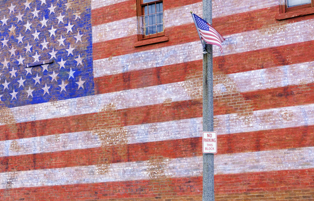 Small-town street scene in Illinois: American flag flapping in breeze by huge painted American flag fading from brick wall